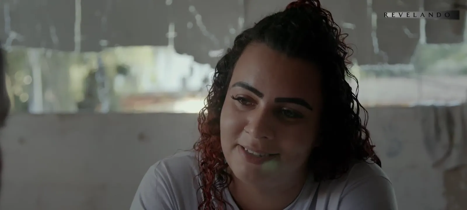 Cristiane Gomes da Silva, mãe de Ana Clara, de cabelo cacheado e camiseta branca, fala com um meio sorriso.